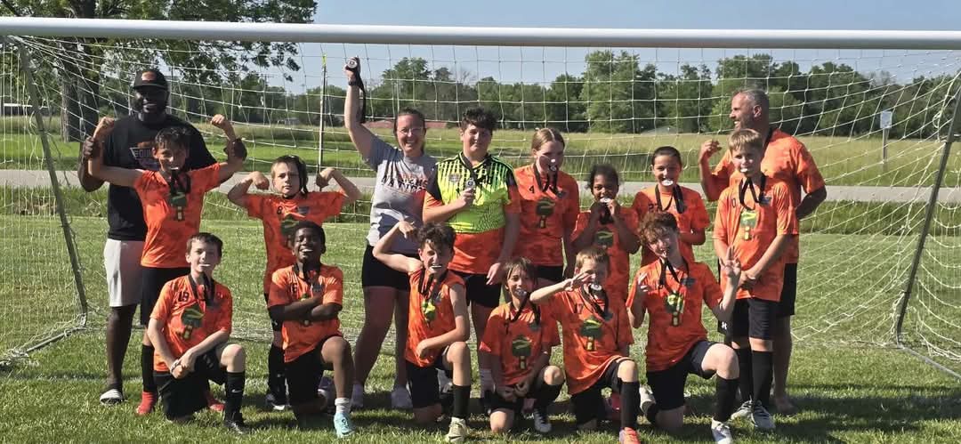 Macon Gunners soccer team is posing with medals. in front of soccer goal.