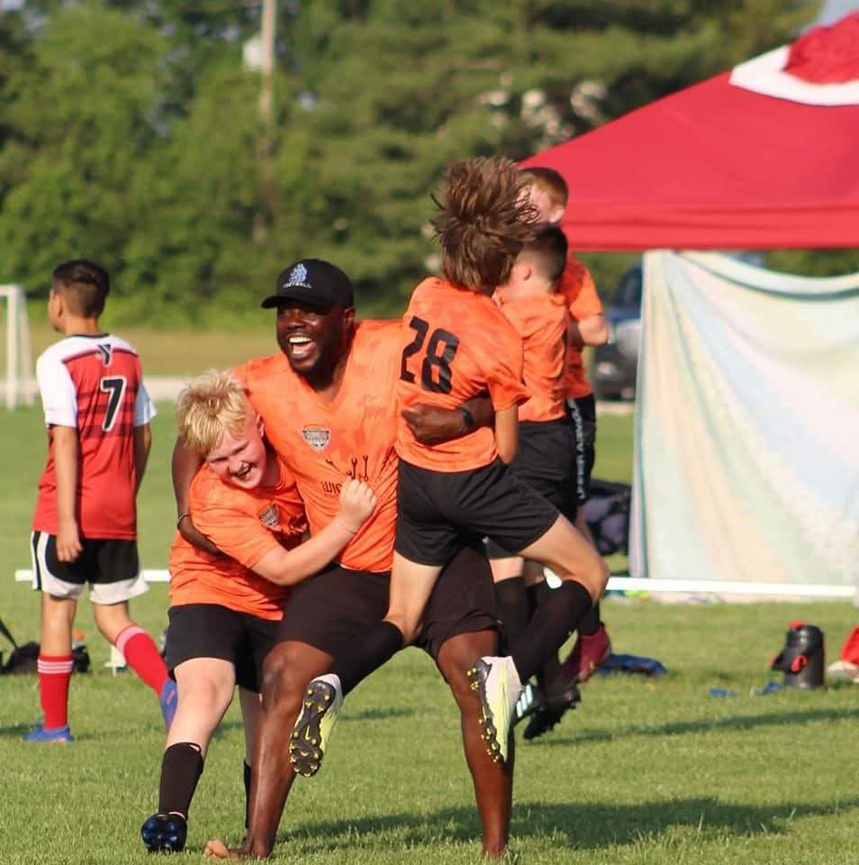Andre celebrating with two youth on soccer field.