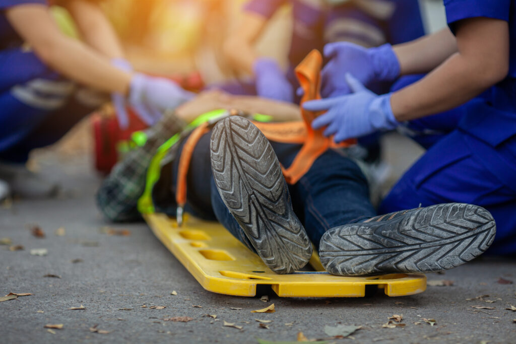 An injured worker lays on a yellow stretcher as EMS personnel provide medical assistance.