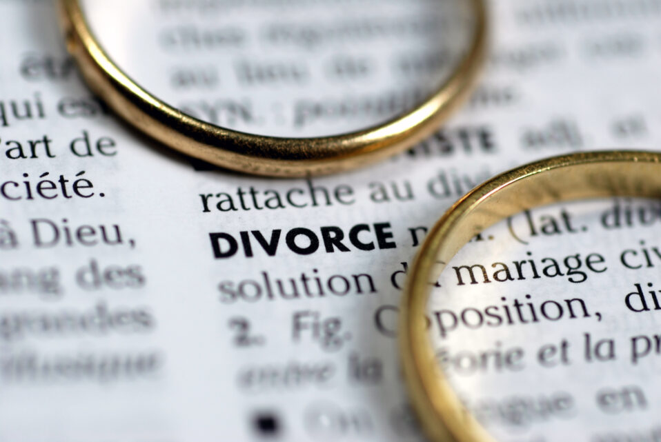 Image of two gold wedding rings sitting on a dictionary page with the word "divorce" and its definition shown.