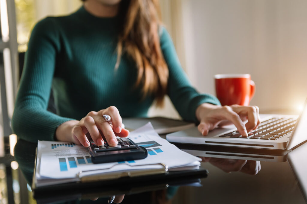 Image of a person using a calculator with one hand and typing on a laptop with the other.