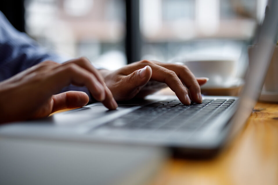 Image of a person typing on a laptop in front of a window.